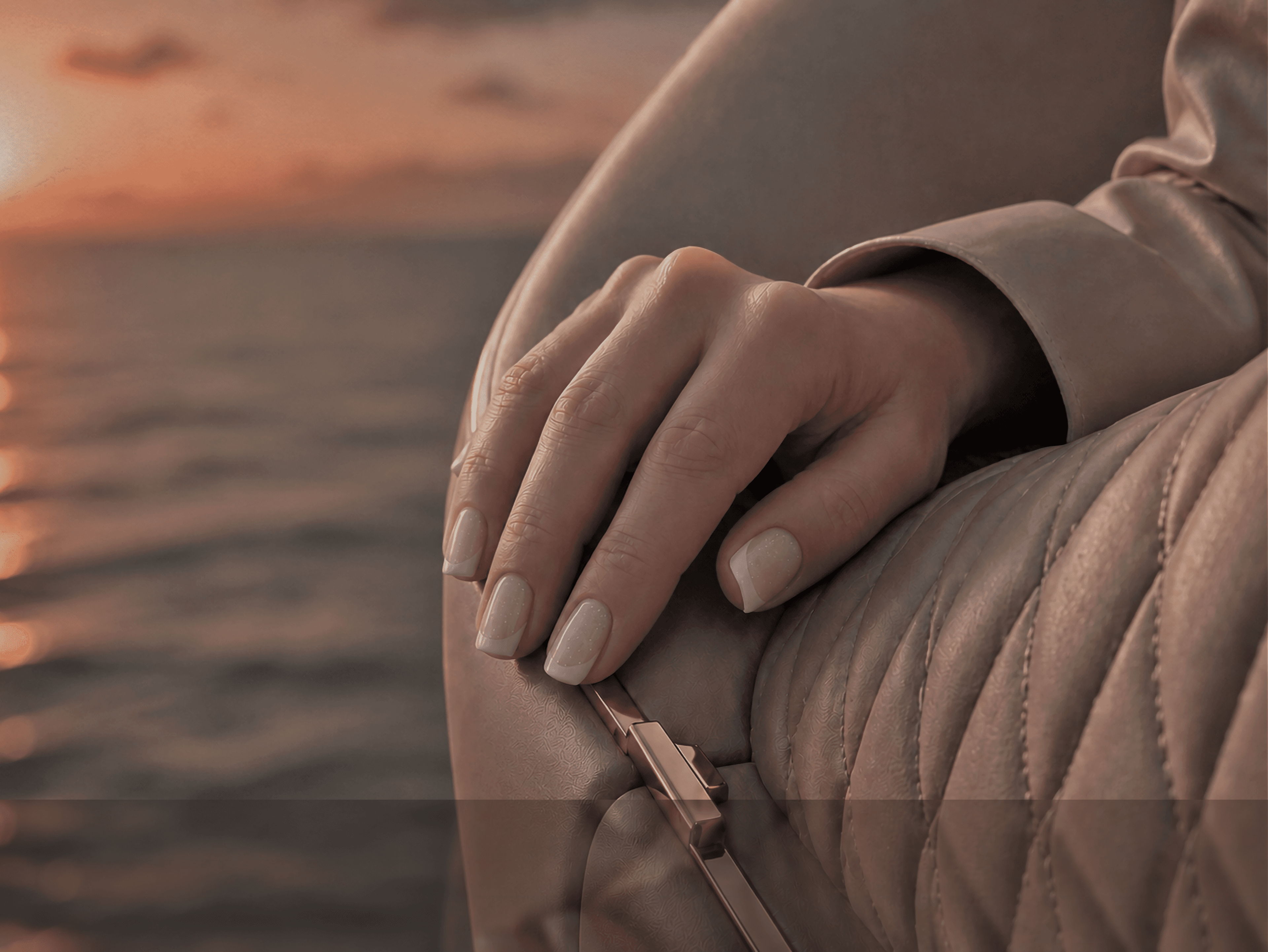 A hand resting on quilted leather above a blurred sea horizon at sunset.